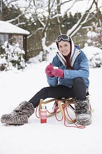 Teenage Girl With Sledge Next To Snowman With Flask And Hot Drink