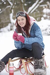Teenage Girl With Sledge Next To Snowman With Flask And Hot Drink