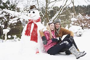 Teenage Couple In Winter Landscape Next To Snowman With Flask And Hot Drink