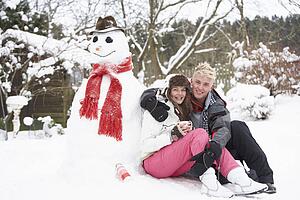 Teenage Couple In Winter Landscape Next To Snowman With Flask And Hot Drink