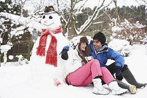 Teenage Couple In Winter Landscape Next To Snowman With Flask And Hot Drink