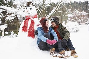 Teenage Couple In Winter Landscape Next To Snowman With Flask And Hot Drink
