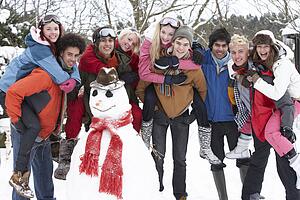 Group Of Teenage Friends Building Snowman In Garden