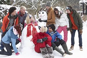 Group Of Teenage Friends Building Snowman In Garden