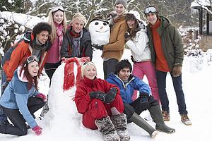 Group Of Teenage Friends Building Snowman In Garden