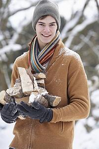 Teenage Boy In Snowy Landscape Carrying Logs