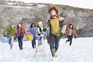 Group Of Teenage Friends Sledging In Snowy Landscape