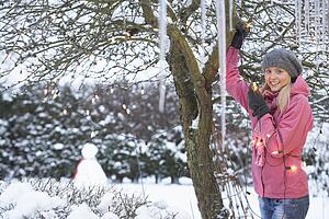 Teenage Girl Hanging Fairy Lights In Tree With Icicles In Foreground
