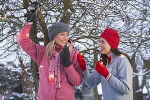 Two Teenage Girls Hanging Fairy Lights In Tree With Icicles In Foreground