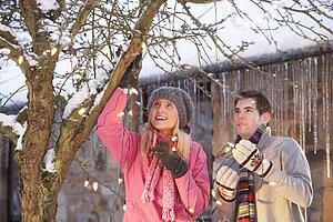 Two Teenage Girls Hanging Fairy Lights In Tree With Icicles In Foreground