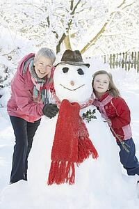 Young Girl With Grandmother Building Snowman In Garden