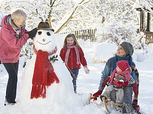 Young Girl With Grandmother And Mother Building Snowman In Garden