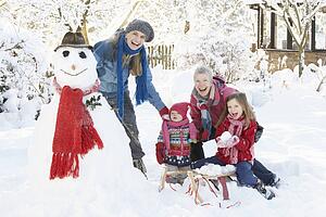 Young Girl With Grandmother And Mother Building Snowman In Garden
