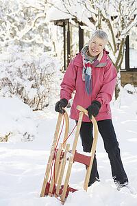 Senior Woman Holding Sledge In Snowy Landscape