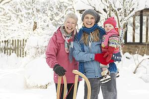 Young Girl With Grandmother And Mother Holding Sledge In Garden