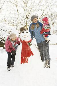 Young Girl With Grandmother And Mother Building Snowman In Garden