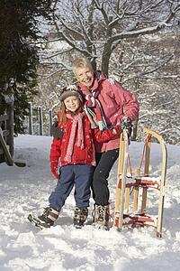 Young Girl With Grandmother Holding Sledge In Snowy Landscape