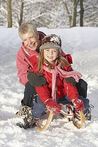 Young Girl With Grandmother Riding On Sledge In Snowy Landscape