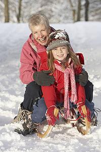 Young Girl With Grandmother Riding On Sledge In Snowy Landscape