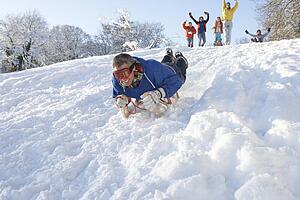 Man Sledging Down Hill With Family Watching
