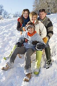 Family Enjoying Sledging Down Snowy Hill
