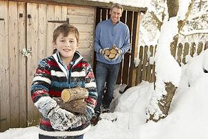 Father And Son Collecting Logs From Wooden Store In Snow