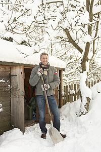 Middle Aged Man Clearing Snow From Path To Wooden Store