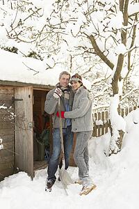 Young Couple Clearing Snow From Path To Wooden Store