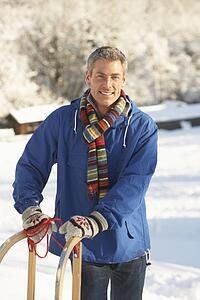 Middle Aged Man Standing In Snowy Landscape Holding Sledge