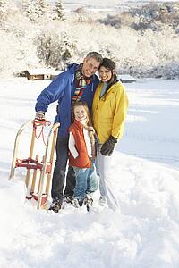 Young Family Standing In Snowy Landscape Holding Sledge