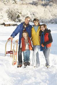 Young Family Standing In Snowy Landscape Holding Sledge
