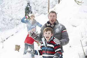 Young Family Having Snowball Fight In Snowy Landscape