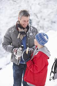 Father And Son Stopping For Hot Drink And Snack On Walk Through Snowy Landscape