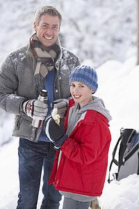 Father And Son Stopping For Hot Drink And Snack On Walk Through Snowy Landscape