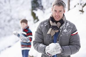 Father And Son Having Snowball Fight In Winter Landscape