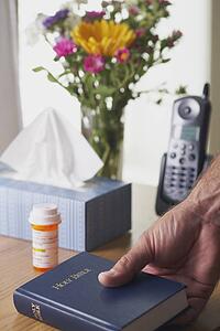 a hand picking up a bible beside a bottle of medication
