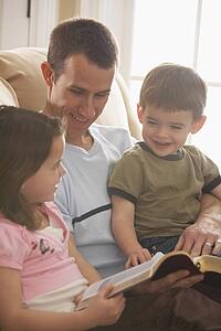 a father reading the bible to his young son and daughter