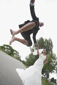 a groom jumping in the air while holding the bride's hand