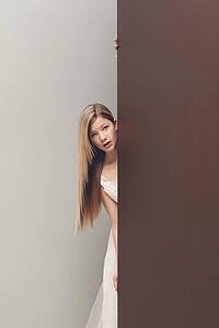 a girl in a white dress looking around the corner