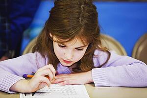 a girl sitting at a table and doing work with a pencil and paper