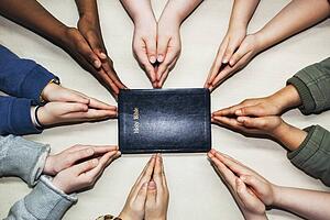 praying hands pointing to a bible