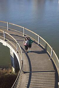 two teenage girls on a pedestrian bridge over a river