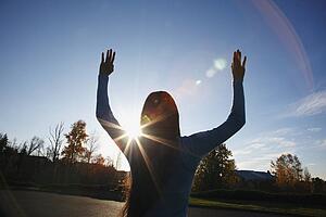 beams of sunlight and a circular glare around a teenage girl with her hands raised