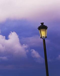 an illuminated lamp post against a cloudy sky