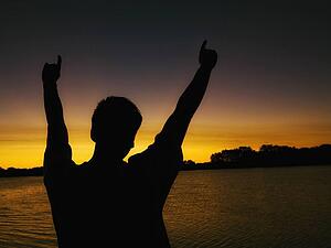 willmar, minnesota, united states of america; silhouette of a man with his arms raised as he watches the sunset over a lake