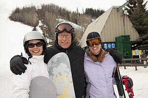 red deer, alberta, canada; three adults at a ski area holding snowboards and skis