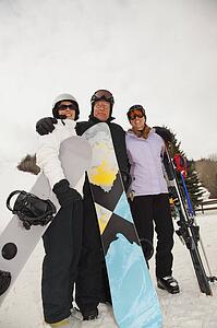 red deer, alberta, canada; three adults at a ski area holding snowboards and skis