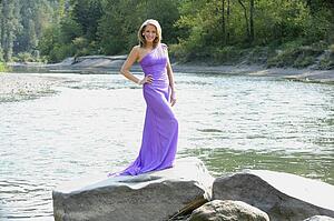 a woman in a formal dress standing on a rock in sandy river; troutdale, oregon, united states of america