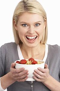 Young Woman Eating Bowl Of Healthy Breakfast Cereal In Studio