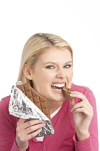 Guilty Looking Young Woman Eating Big Bar Of Chocolate In Studio